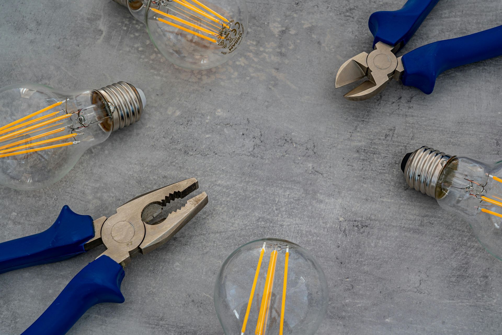 Lightbulbs and pliers arranged on a gray surface, suggesting electrical work.
