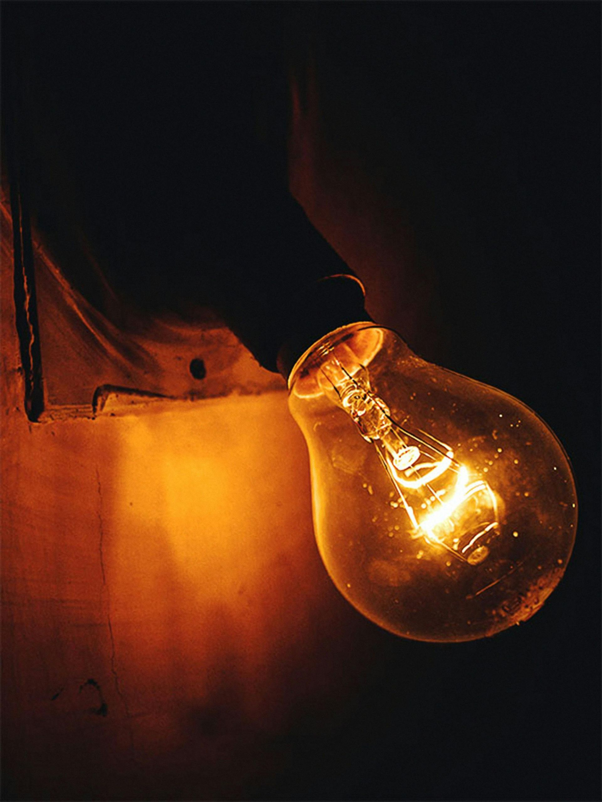 Glowing lightbulb in a dark room, illuminating a wall and casting warm light.