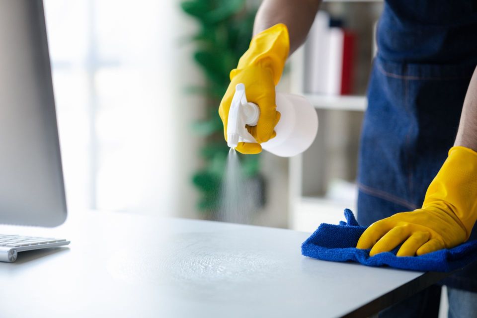 A person wearing yellow gloves is cleaning a desk in front of a computer.