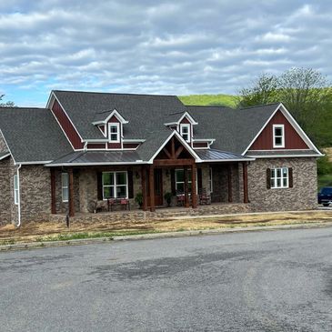 A large brick house with a porch and a gray roof is sitting on the side of the road.