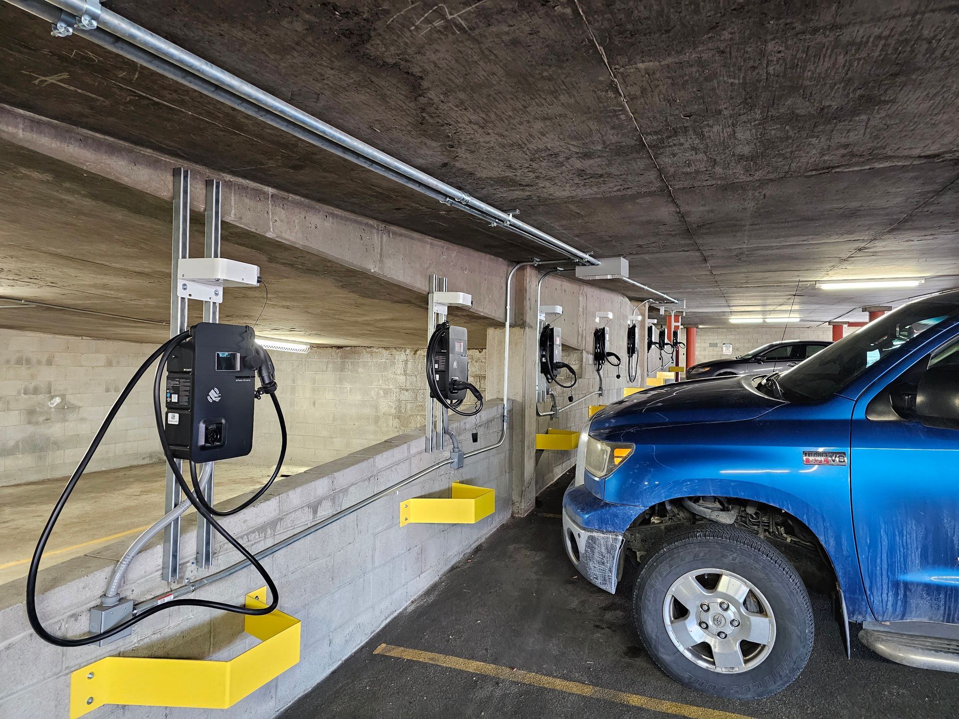 Electric vehicle charging stations in an underground parking garage. Blue truck parked in front.