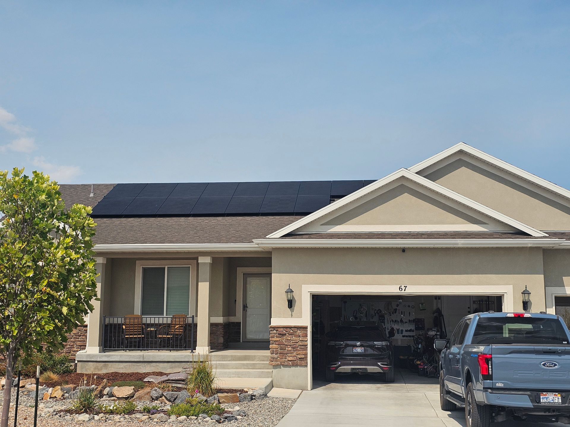 House with solar panels on the roof, a garage with a car, and a truck parked outside on a sunny day.
