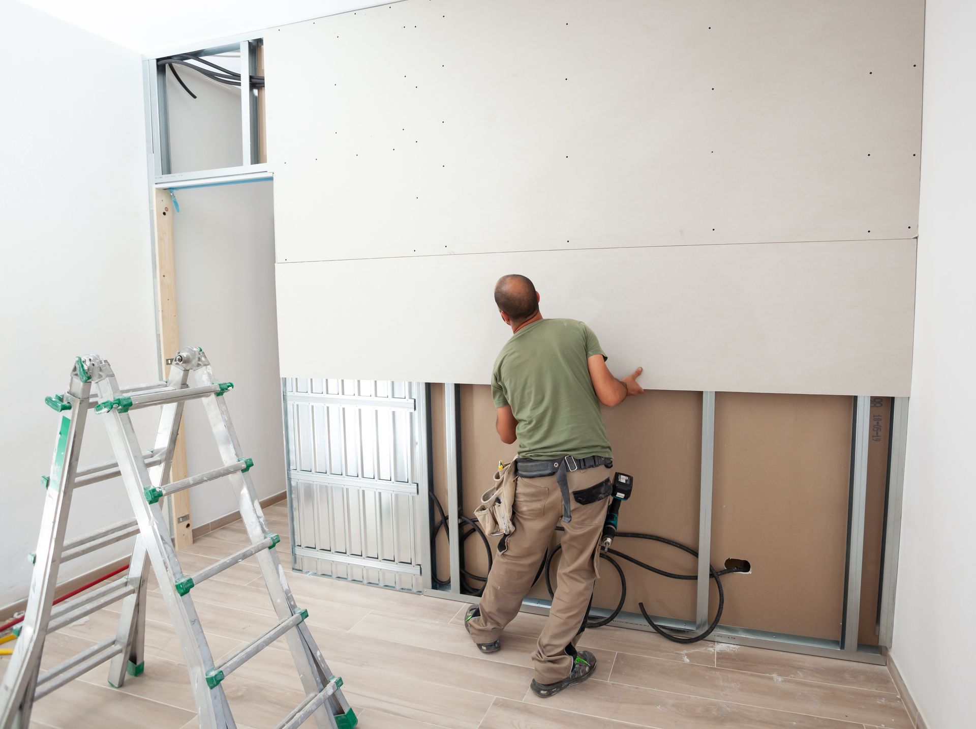 A man is working on a wall in a room with a ladder.