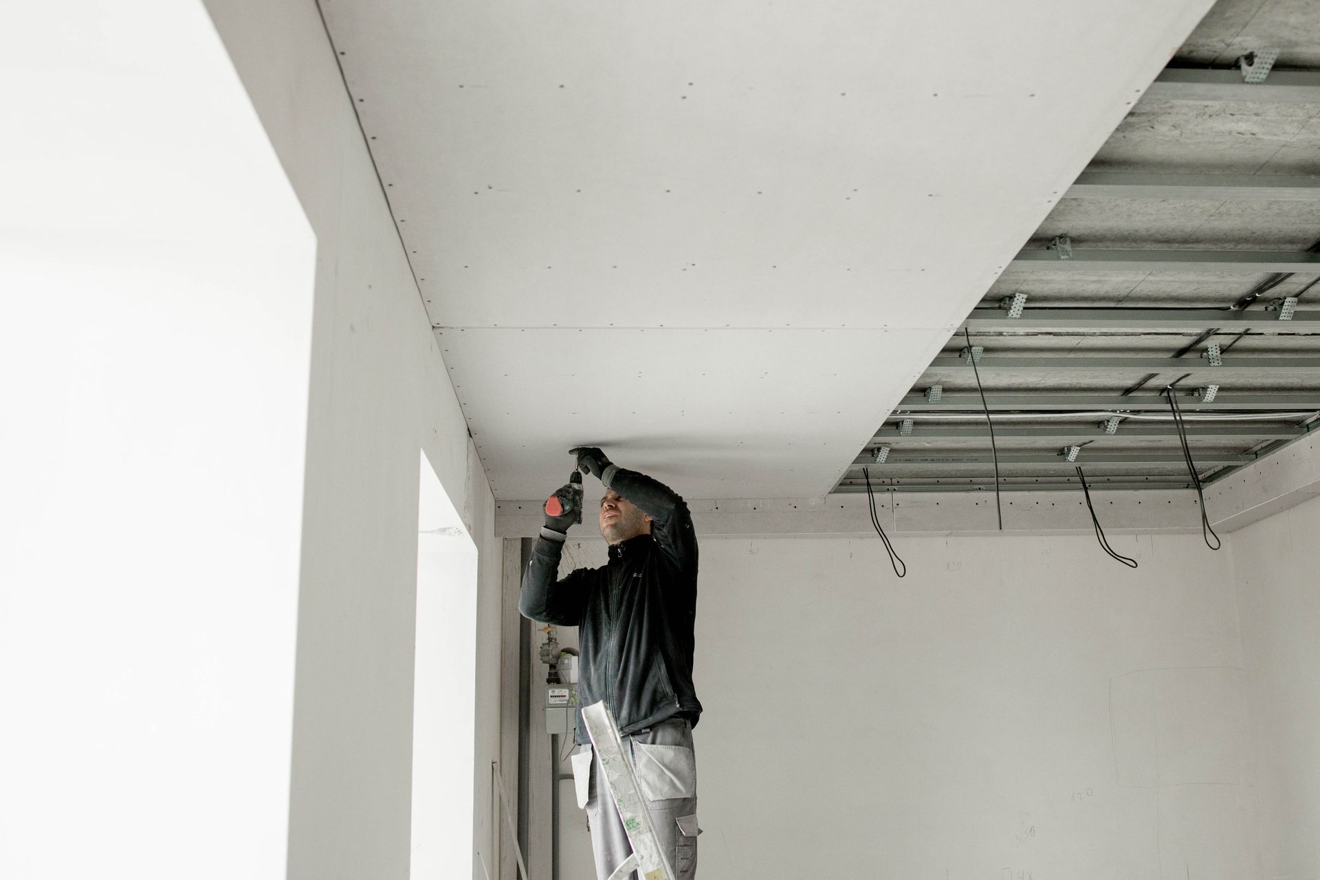 A man is standing on a ladder working on a ceiling.