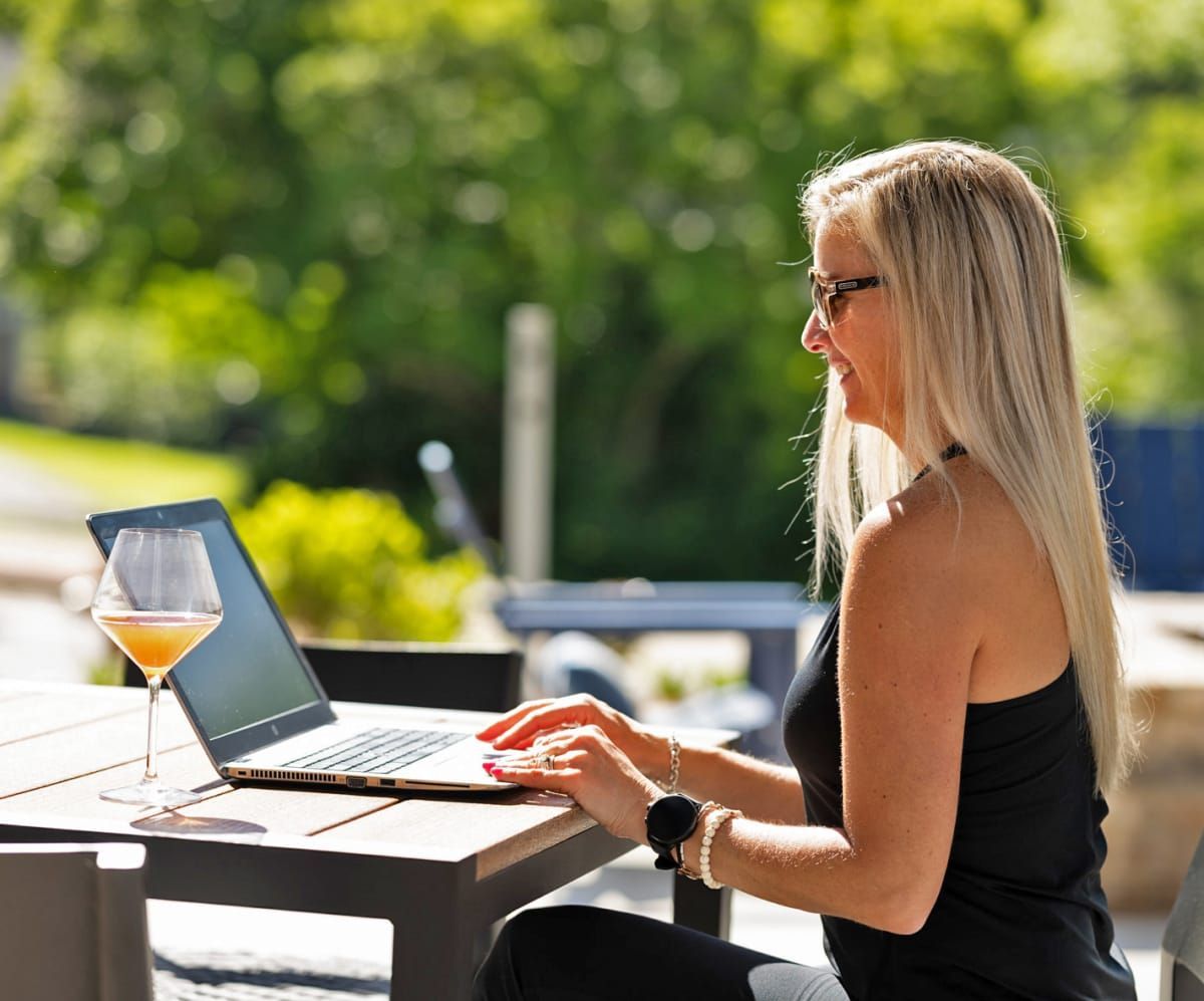 A woman is sitting at a table with a laptop and a glass of wine.