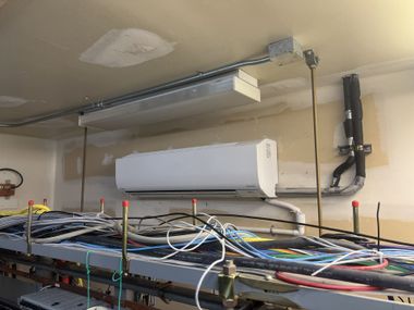 Wall-mounted HVAC unit above a cluttered electronics rack with many cables and wires under it