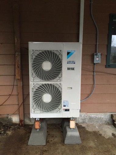 Outdoor Mitsubishi HVAC unit on cinder blocks against a brick wall with exposed pipes and wiring.