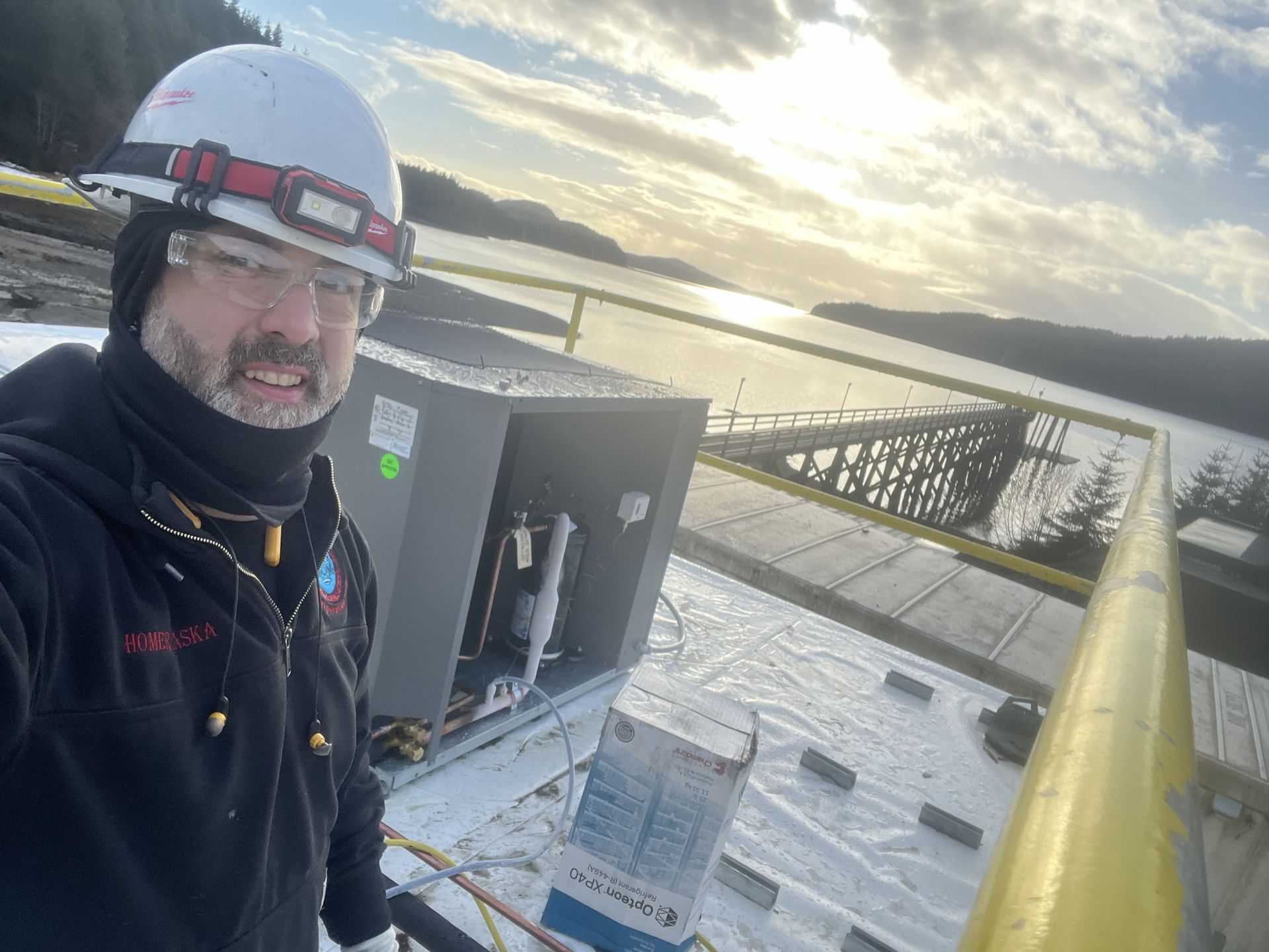 Worker in hard hat on a rooftop, with waterfront and bridge in the background.