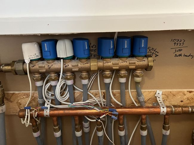 Water manifold with blue and white valves and tubing mounted on a wall under a shelf