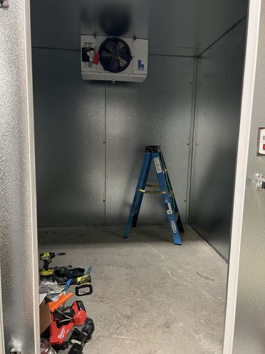 Small empty utility room with a blue ladder, wall-mounted unit, and tools on the floor.