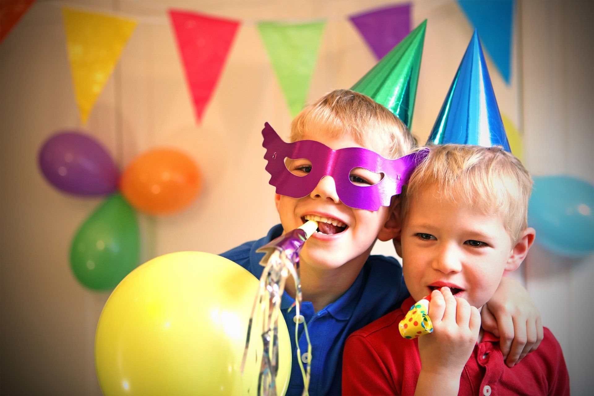 two young boys wearing party hats and masks are blowing party horns at a birthday party .