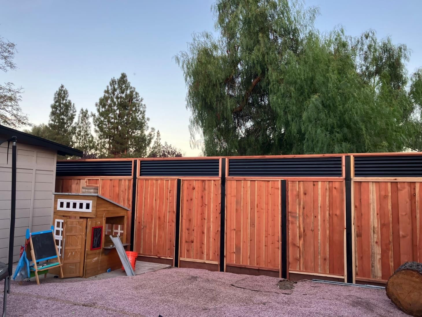 Person using a power tool to sand and polish an aging wooden fence, giving it a renewed appearance.