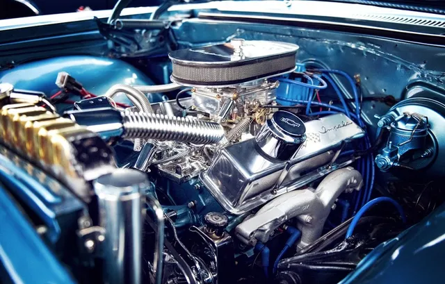 Blue engine of a classic car, with chrome parts and wiring, in a well-lit setting.