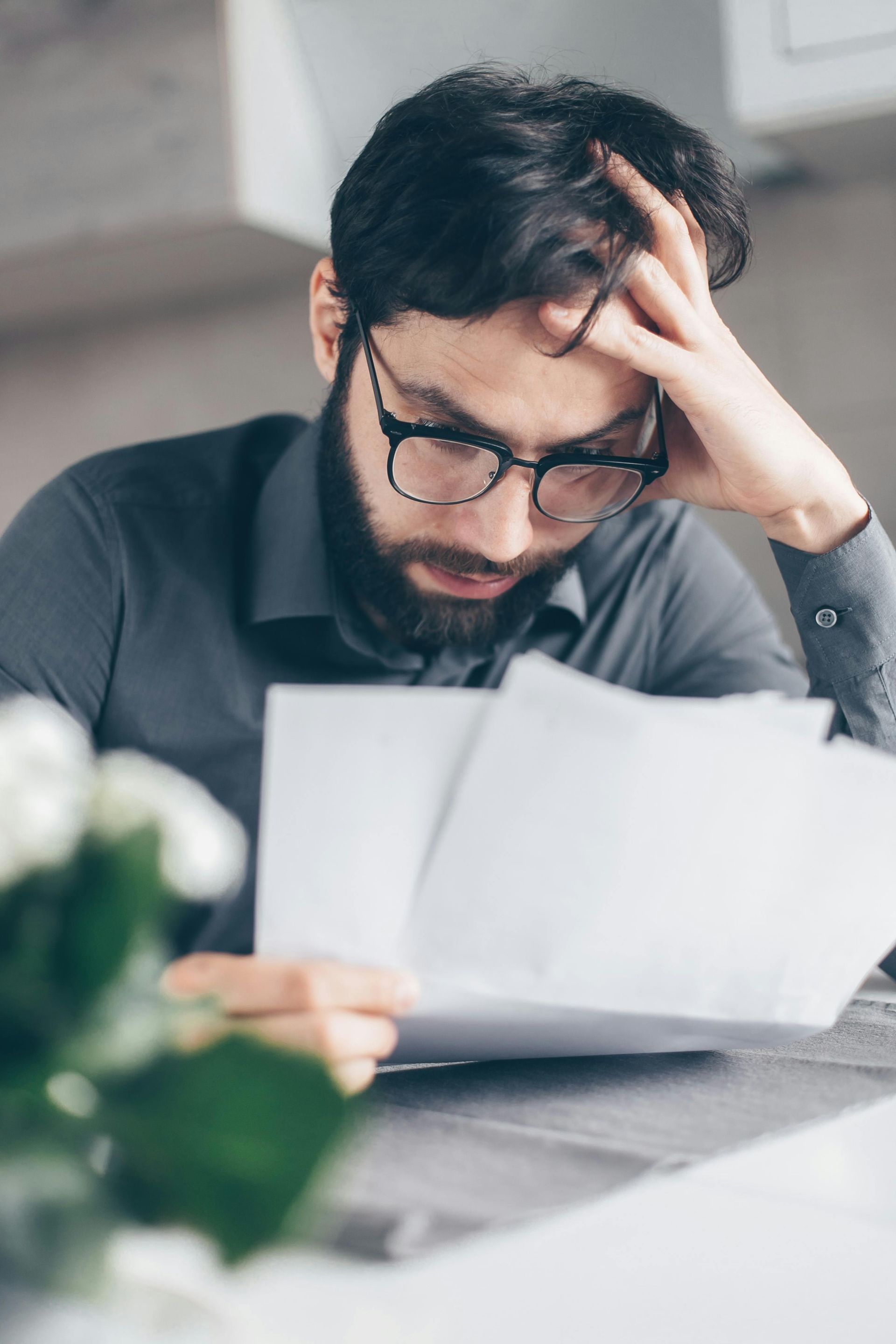 Man with glasses holds papers, appears stressed, indoors.