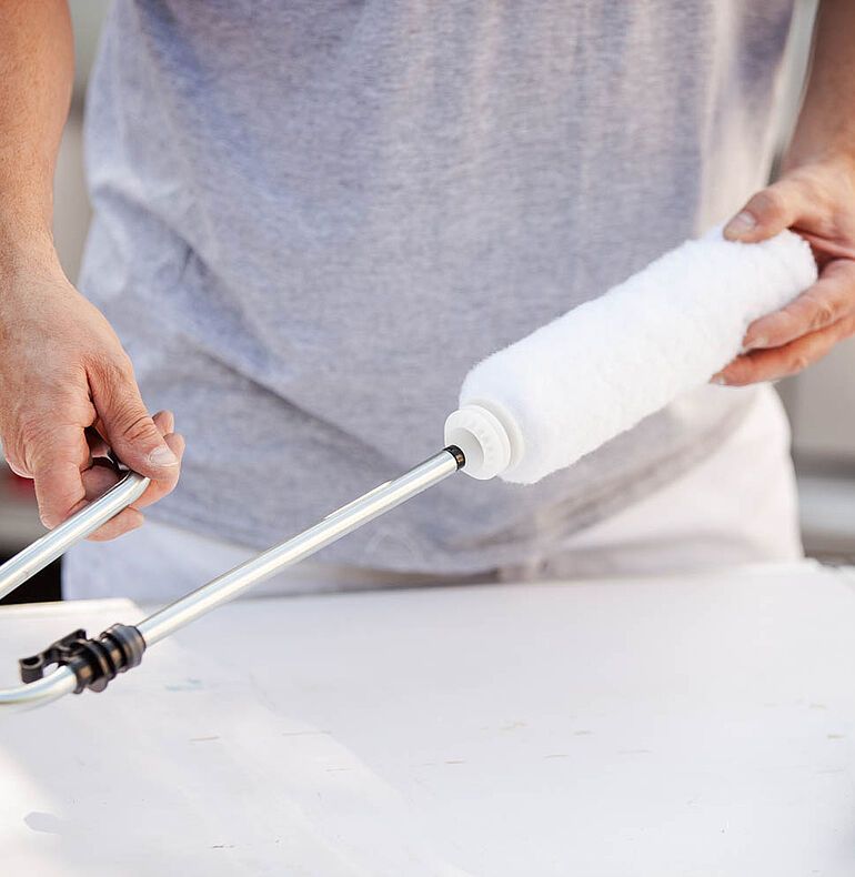 Man scattering flakes in a garage. Beige walls, concrete floor, blue buckets.