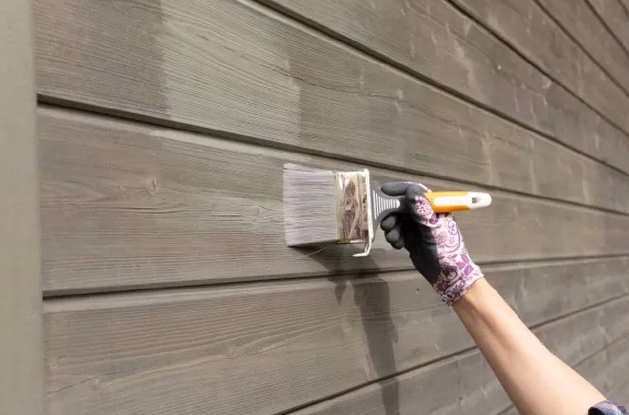 A person painting a wooden exterior wall with a brush.