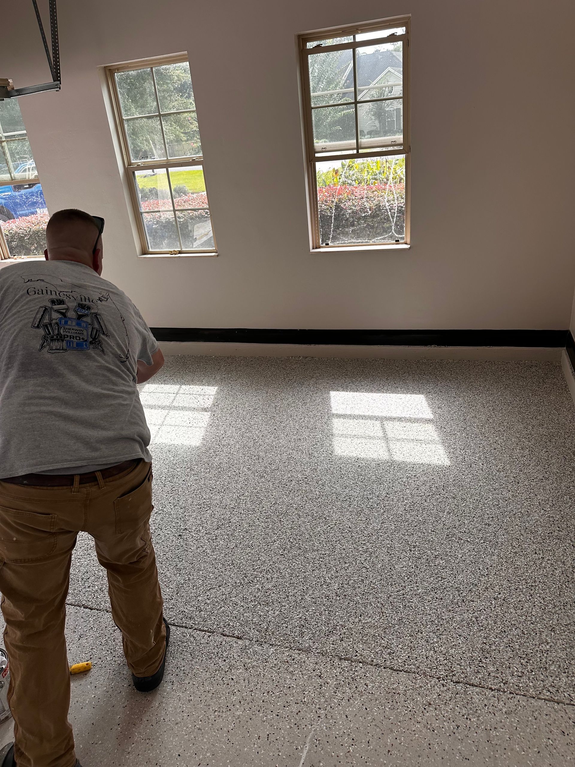 Man installing epoxy floor coating in garage with windows.