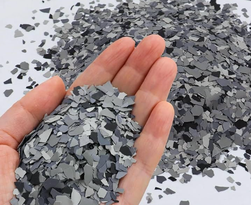 Hand holding gray and dark gray paint flakes against a white background.