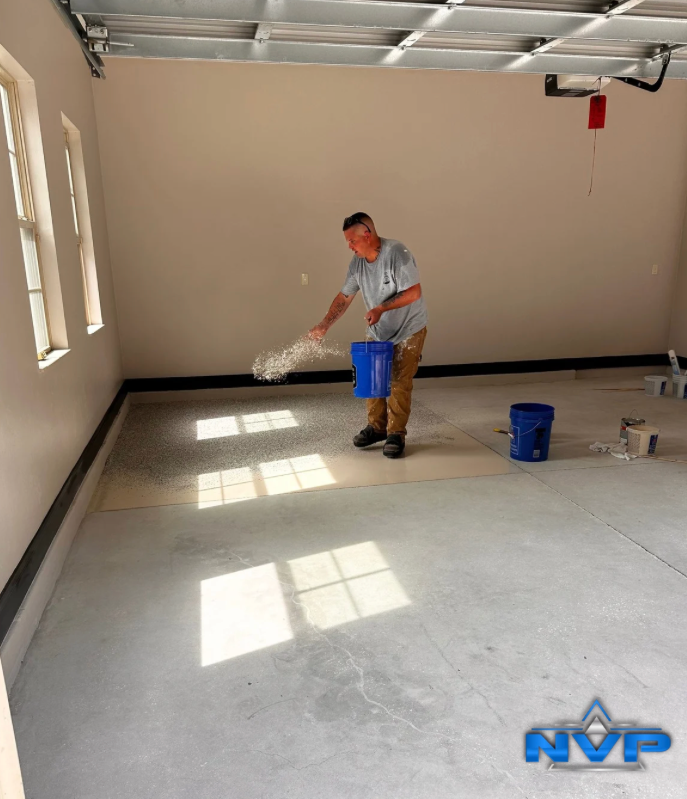 Man scattering flakes in a garage. Beige walls, concrete floor, blue buckets.