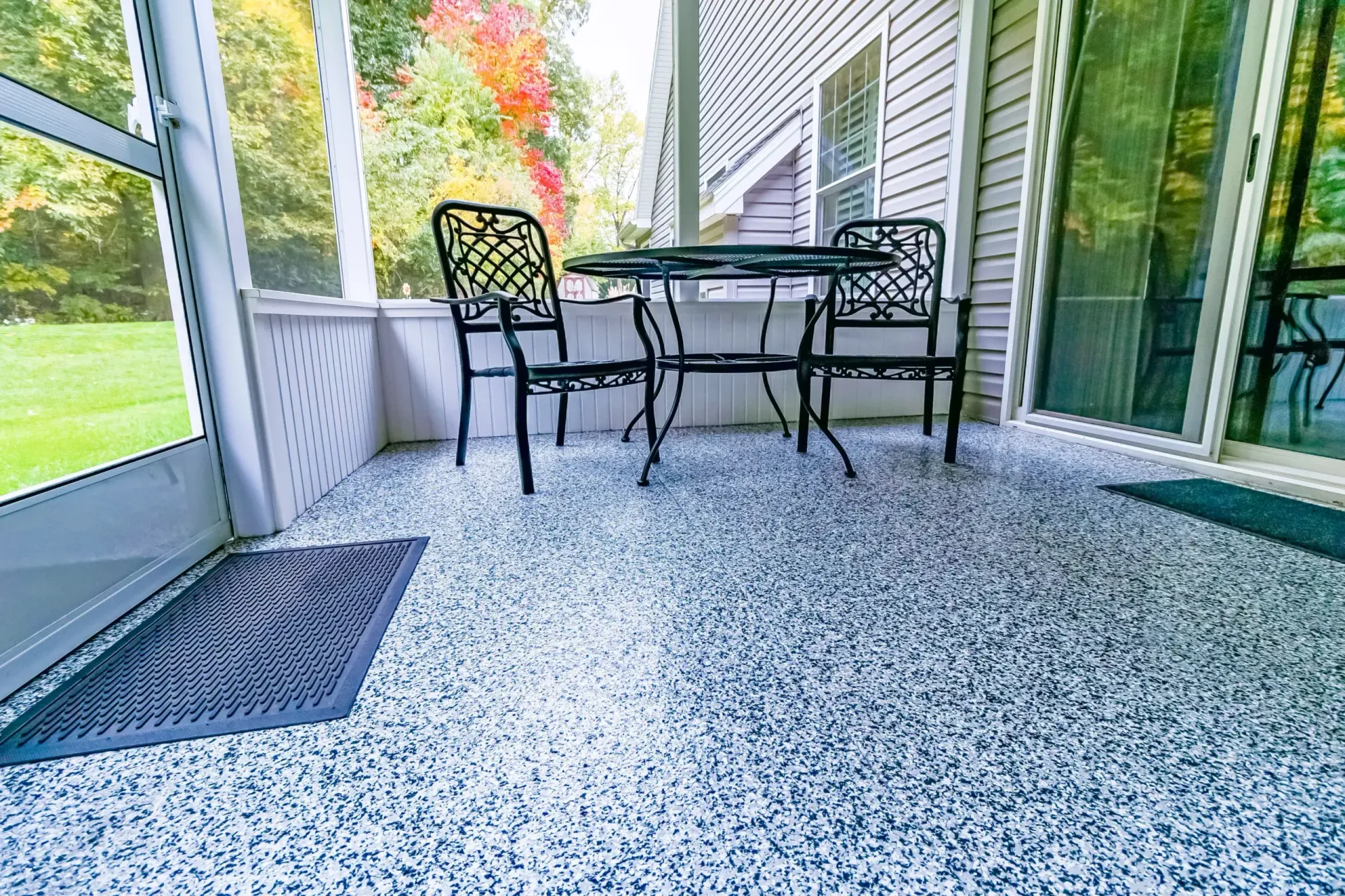 Screened porch with black table and chairs, textured blue and white floor, and a doormat.