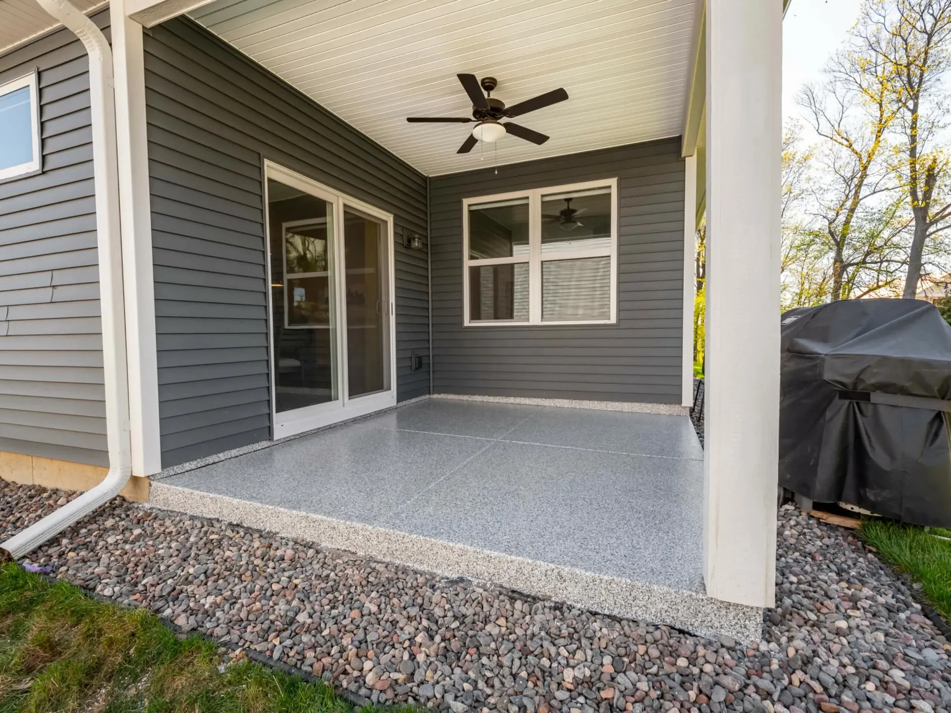 Covered patio with gray floor, dark siding, white columns, and a ceiling fan.