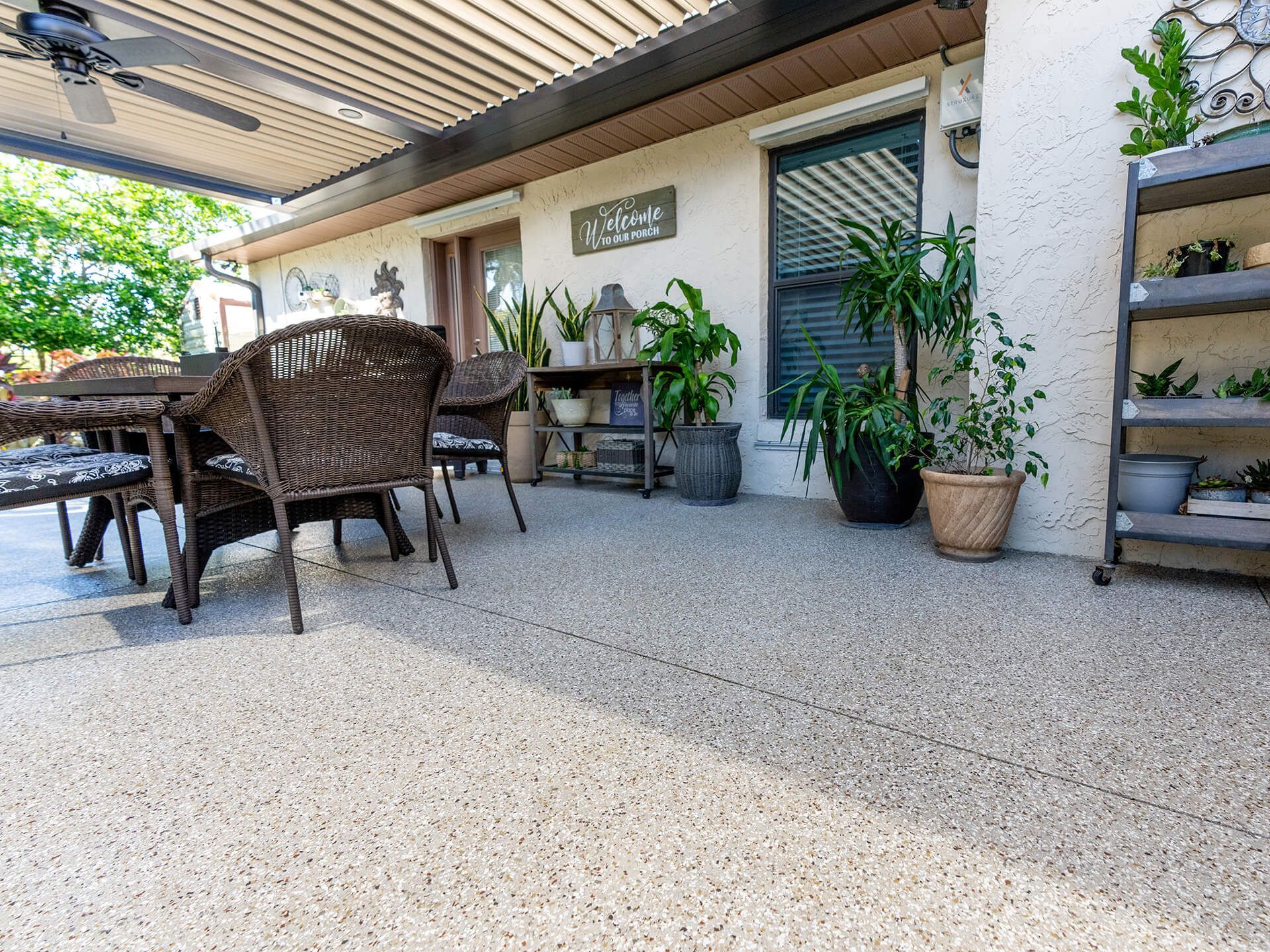 Patio with stone floor, wicker furniture, and plants under a covered pergola.