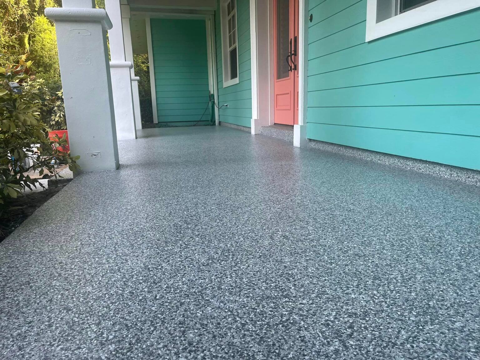 Covered porch with a speckled gray floor, turquoise siding, and a pink door.