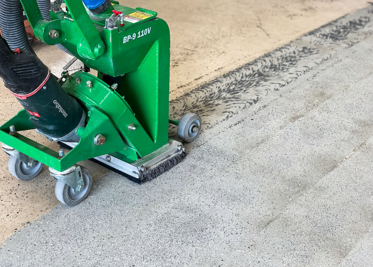 Green floor grinding machine removing epoxy coating from a concrete surface.