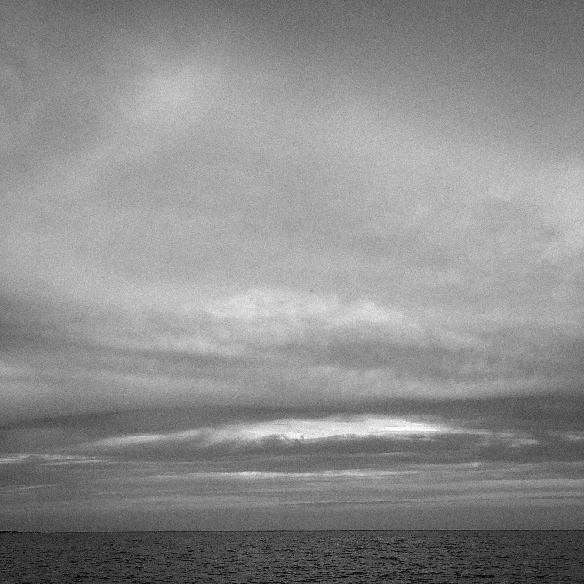 A black and white photo of a cloudy sky over the ocean
