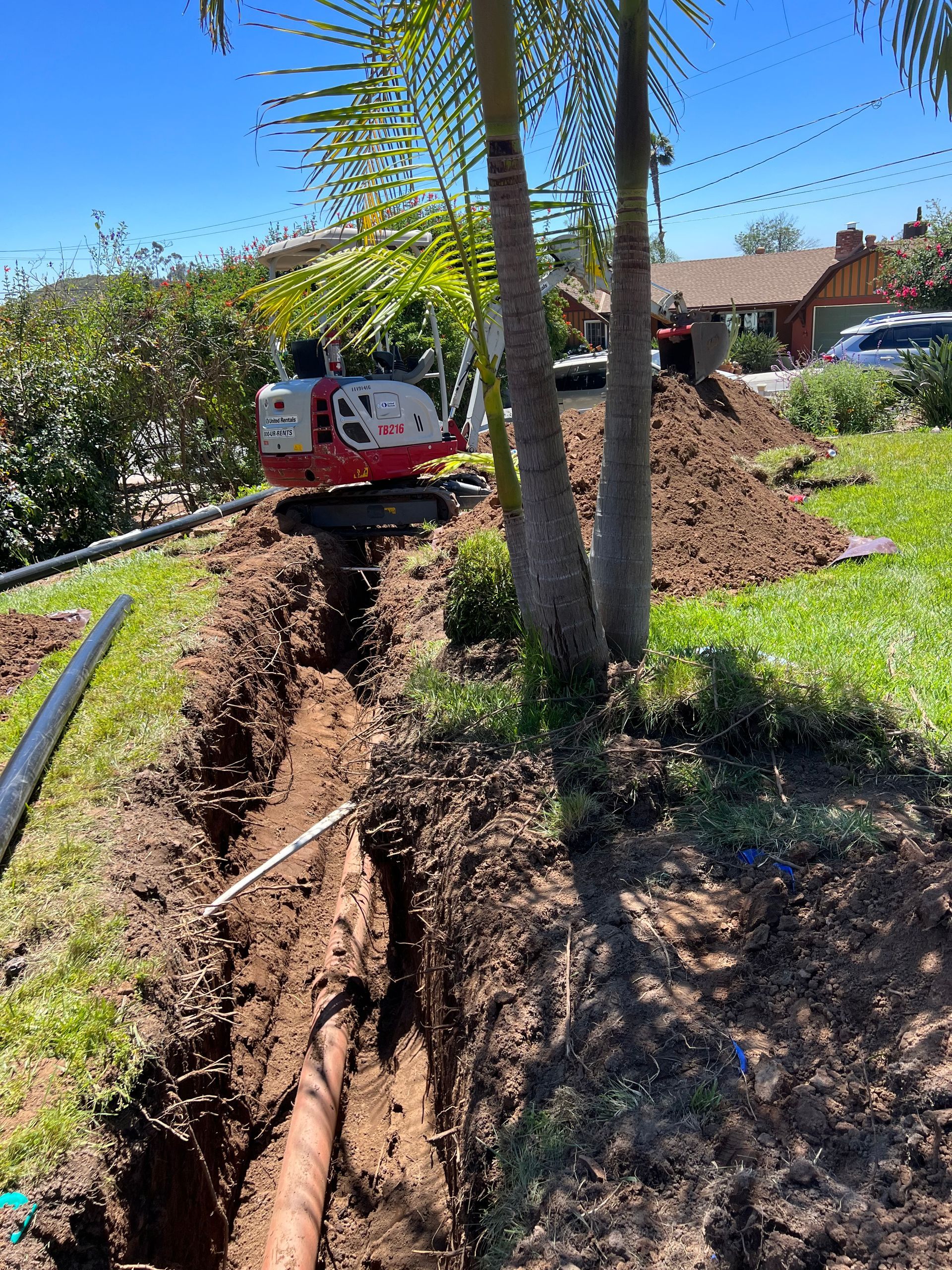 An excavator is digging a hole in the ground in a yard.