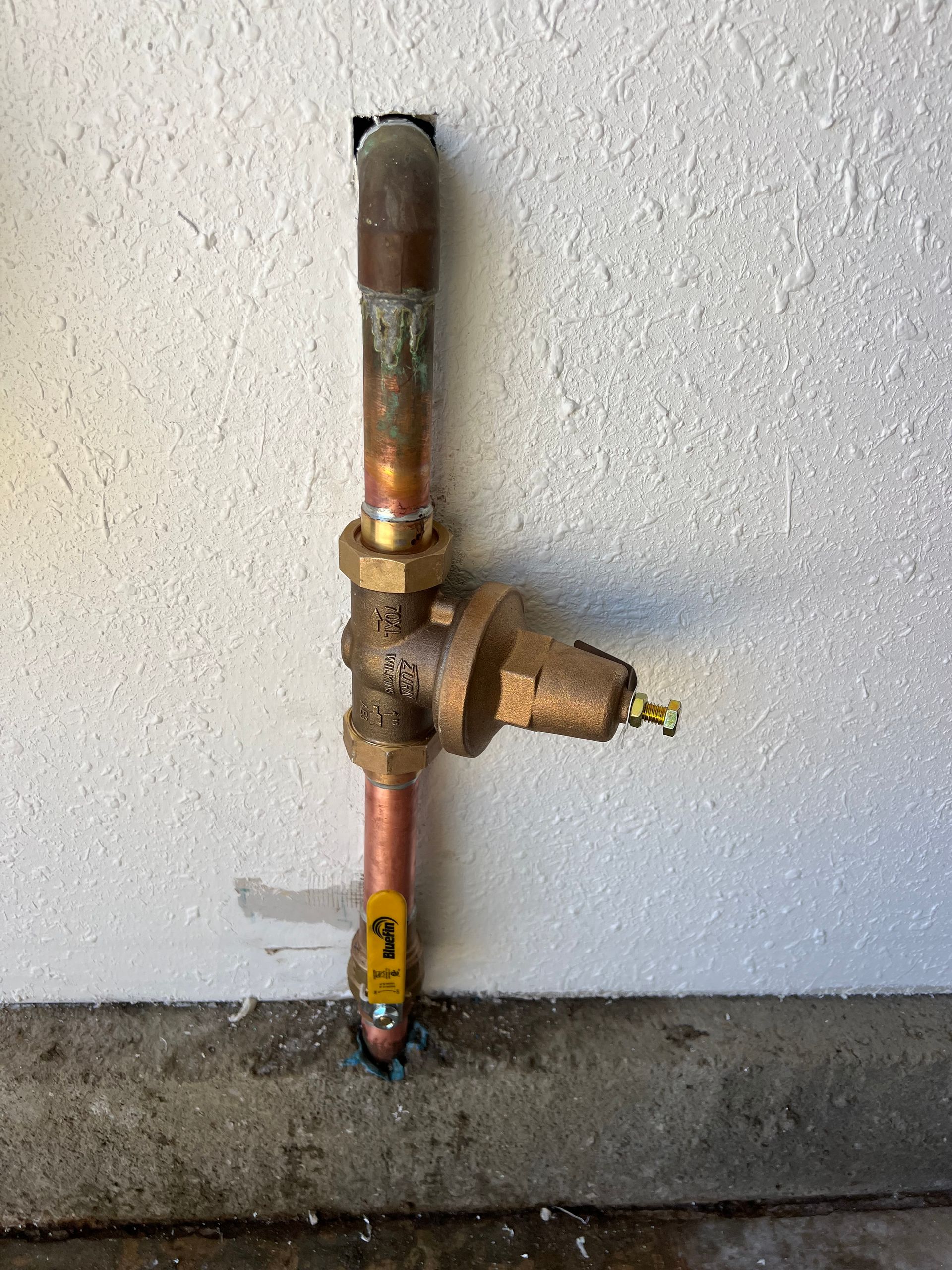 Copper water pressure regulator pipe against a textured white wall.