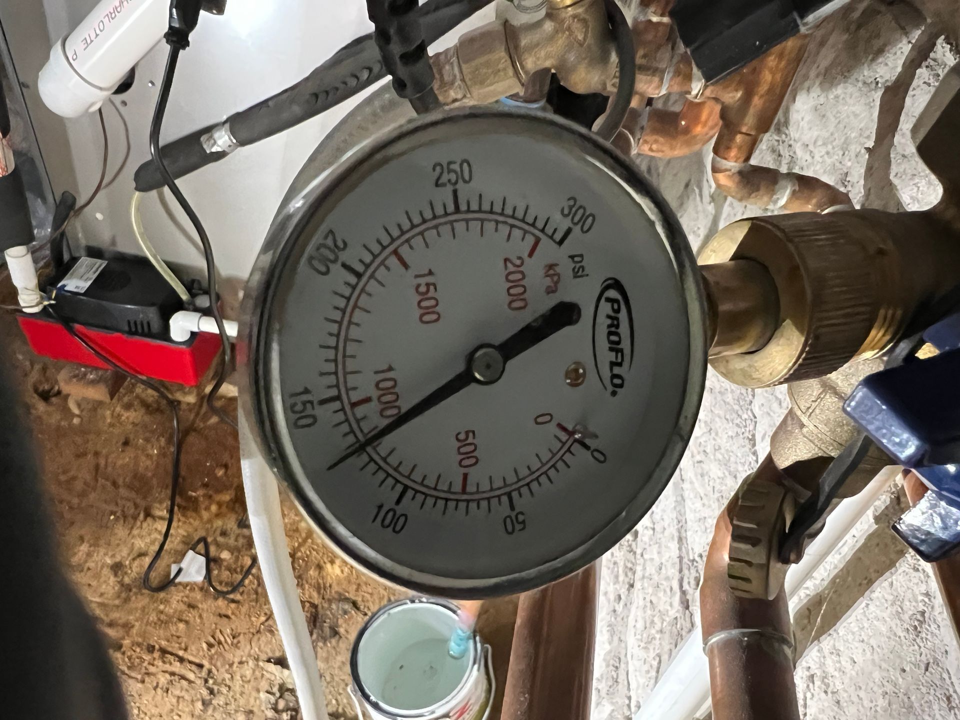 Pressure gauge showing 700 psi, connected to copper pipes and plumbing in a basement.