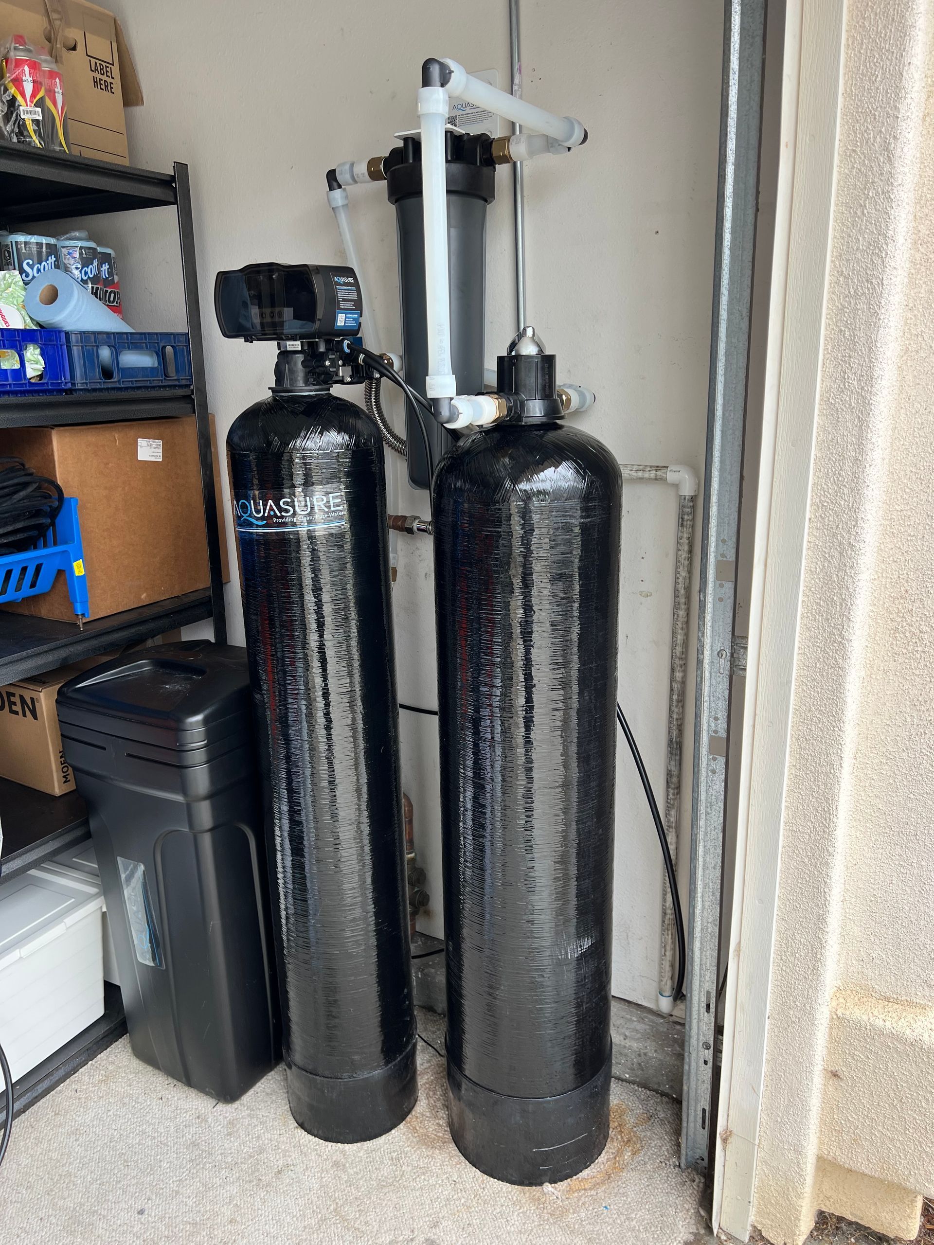Two black water filtration tanks with a filter unit, next to a garage wall, and storage.