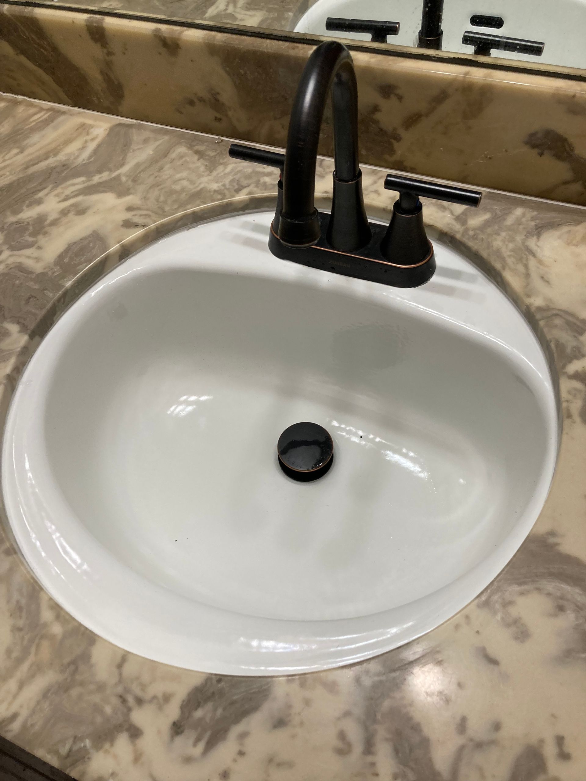 White oval bathroom sink with a dark faucet and a stone countertop.