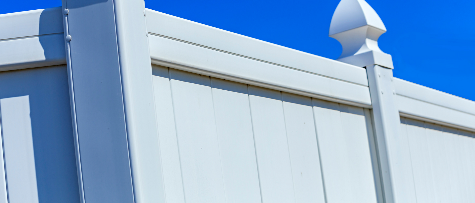 White vinyl fence against a bright blue sky.
