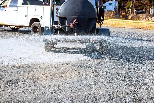 A person’s hands holding a large industrial nozzle, spraying a thick stream of teal-colored hydroseed mulch onto the ground.