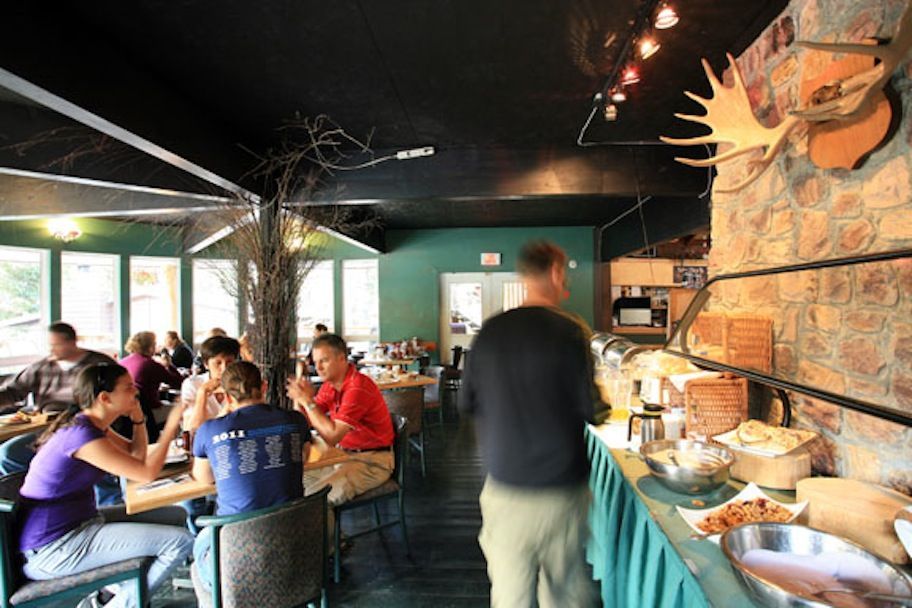Restaurant interior with patrons at tables, buffet, and moose antlers on a stone wall.