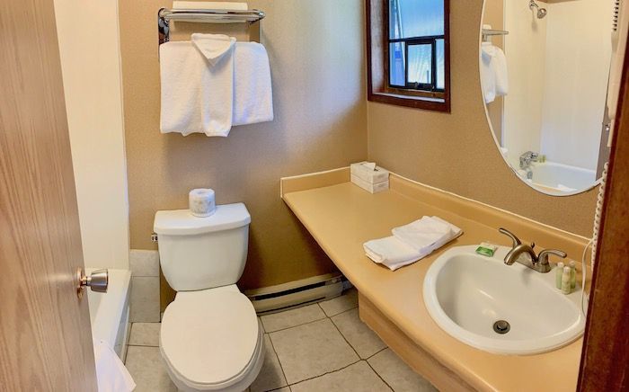 Bathroom with a toilet, sink, mirror, towels, and a small window.
