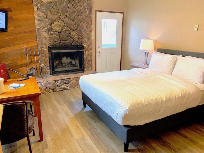 Cozy hotel room with stone fireplace, queen bed, small table, and door.