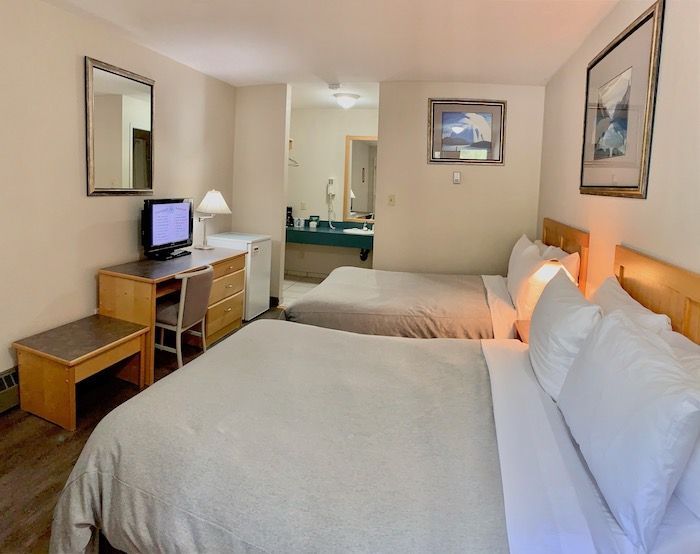 Motel room with two beds, desk with TV, and a view into the bathroom.