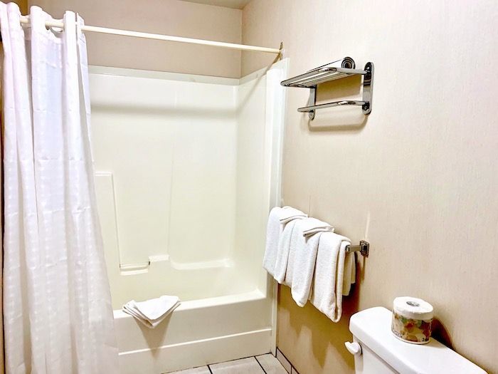 Bathroom with white shower and curtain, toilet, towel rack with towels.
