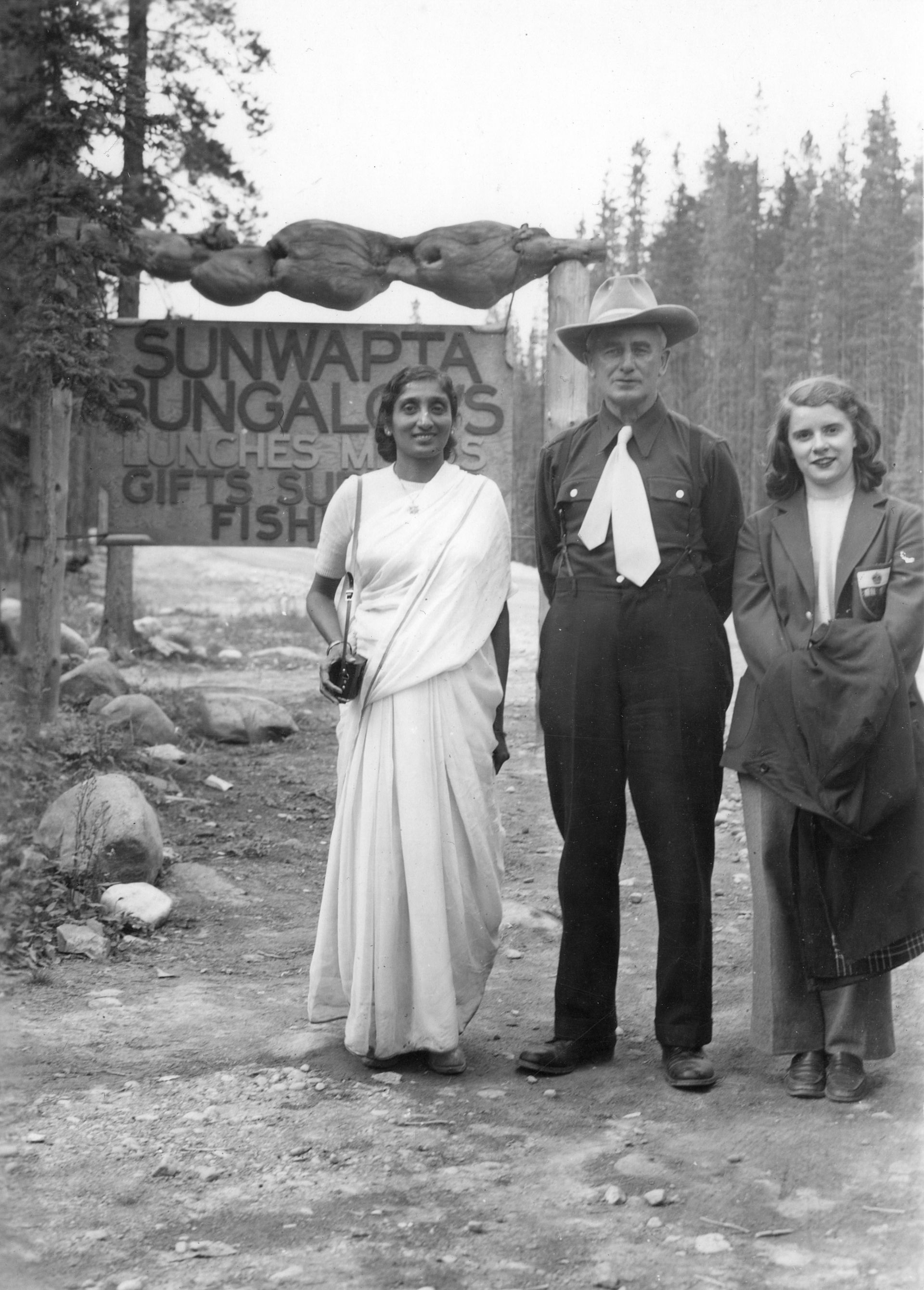Three people stand by a sign for Sunwapta Bungalows. A person in a sari holds a camera.