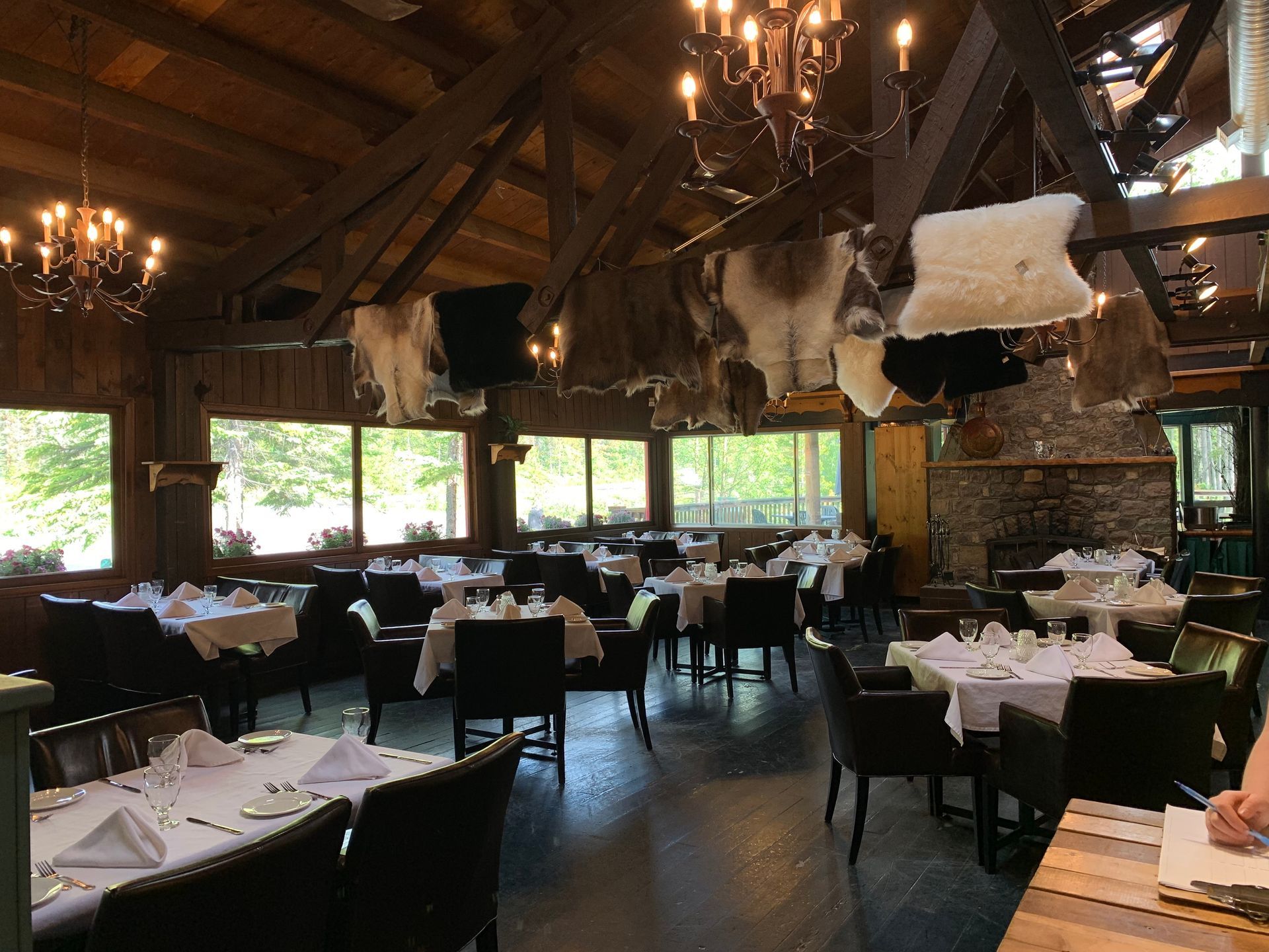 Restaurant interior with tables set for dining, rustic decor, exposed wooden beams, and chandeliers.