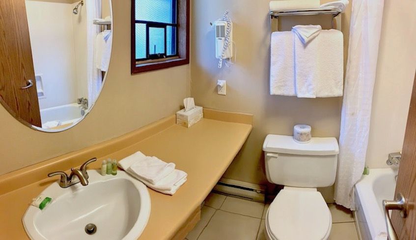 Bathroom with white sink, toilet, tub, and towels; tan countertop and walls; small window.