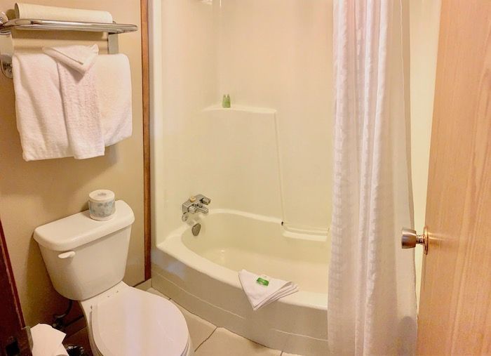 Small bathroom with toilet, bathtub/shower, towels, and closed door.