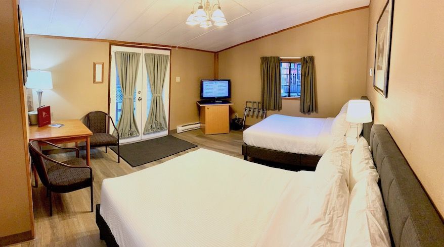 Hotel room with two beds, small table, TV, and French doors leading outside.