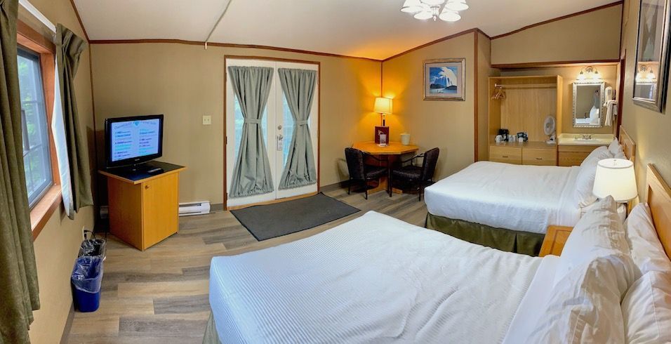 Hotel room with two beds, TV, table, and a door leading outside.