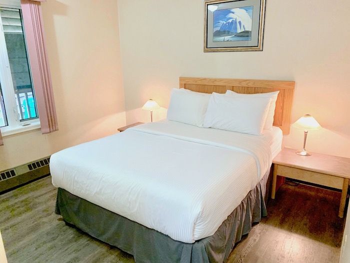 Bedroom with double bed, two nightstands with lamps, window with pink curtain, framed artwork.