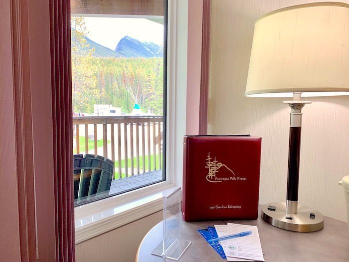 Interior hotel room with mountain view, red binder on table next to lamp, window with balcony.