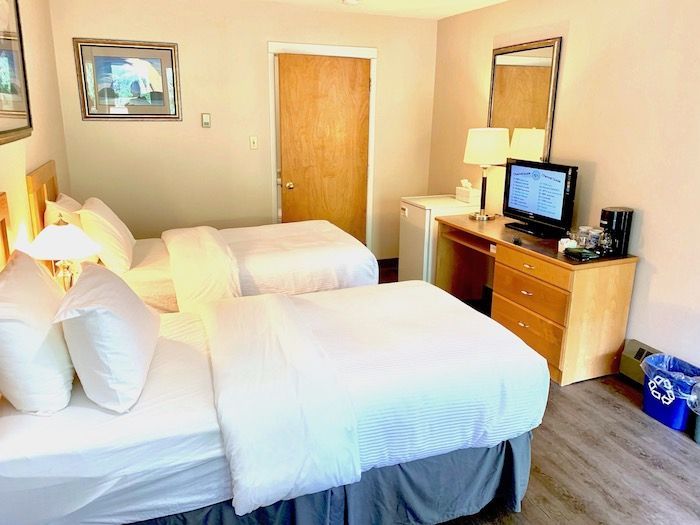 A hotel room with two beds, a desk, a TV, and a mini-fridge.